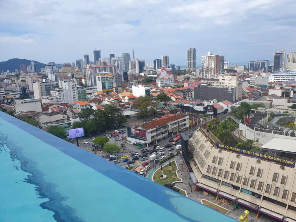 A cityscape view of George Town, Penang, showing busy streets, colorful rooftops, and modern skyscrapers as seen from the infinity pool at The Granite Luxury Hotel.