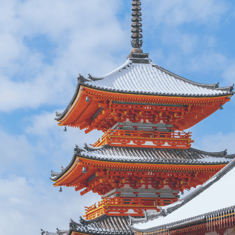 Bright red pagoda of Kiyomizu-dera temple covered in fresh snow under a clear blue sky, showcasing traditional Japanese architecture in winter.