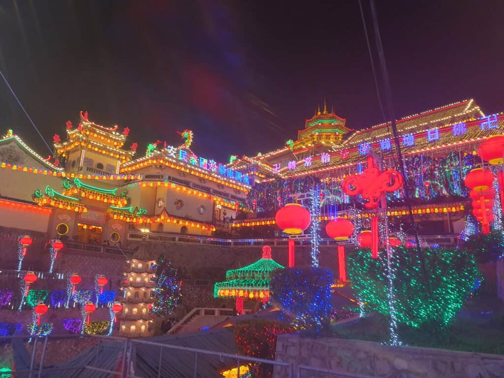 A dazzling night view of Kek Lok Si Temple in Penang, Malaysia, fully illuminated with colorful neon lights and decorated with rows of glowing red lanterns.
