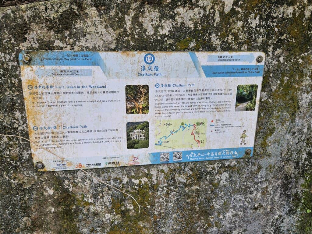 An aged informational sign about Chatham Path, mounted on a mossy rock, featuring English and Chinese text, a map of the trail, historical facts, and small images of a mansion and woodland.
