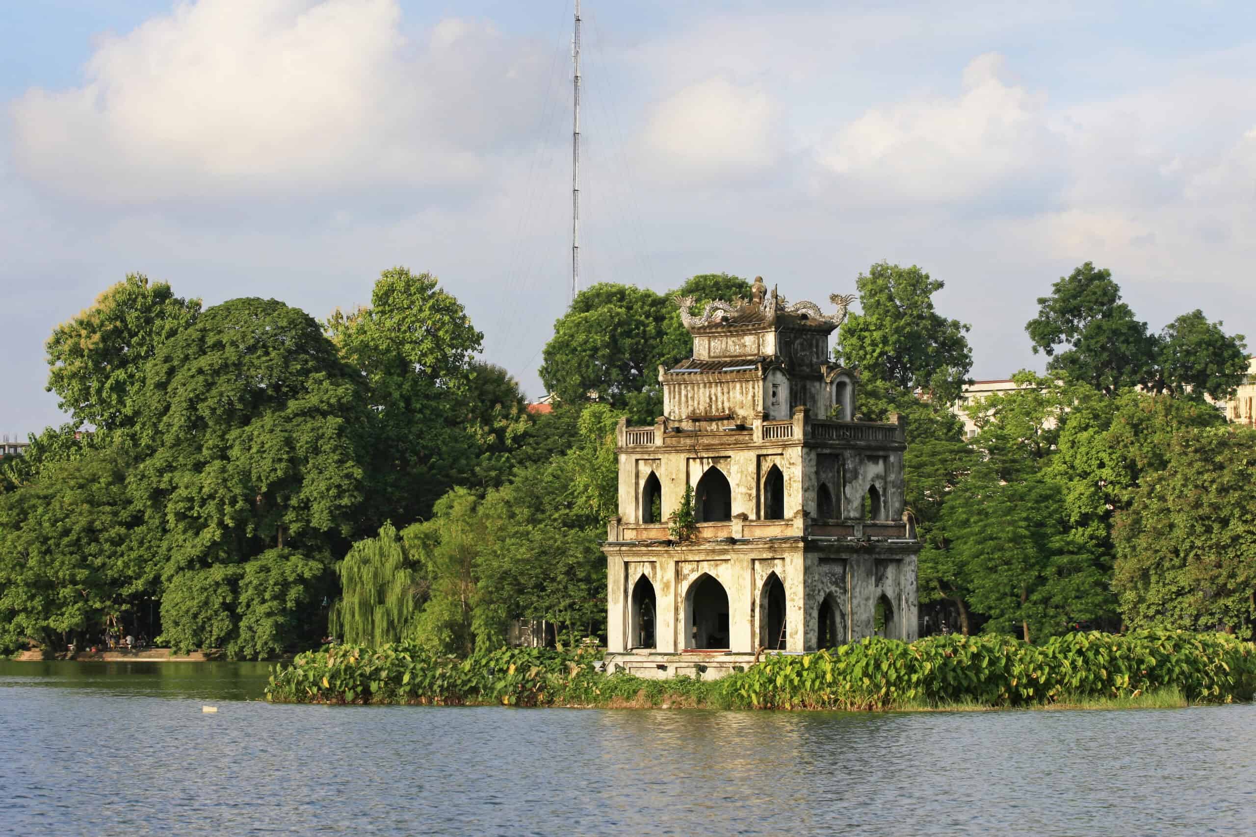 The Turtle Tower, a small three-tiered pagoda with weathered stone walls, stands on a lush islet in the middle of Hanoi’s Hoàn Kiếm Lake. Surrounded by calm water and dense green trees, the tower is a peaceful and iconic symbol of the city.