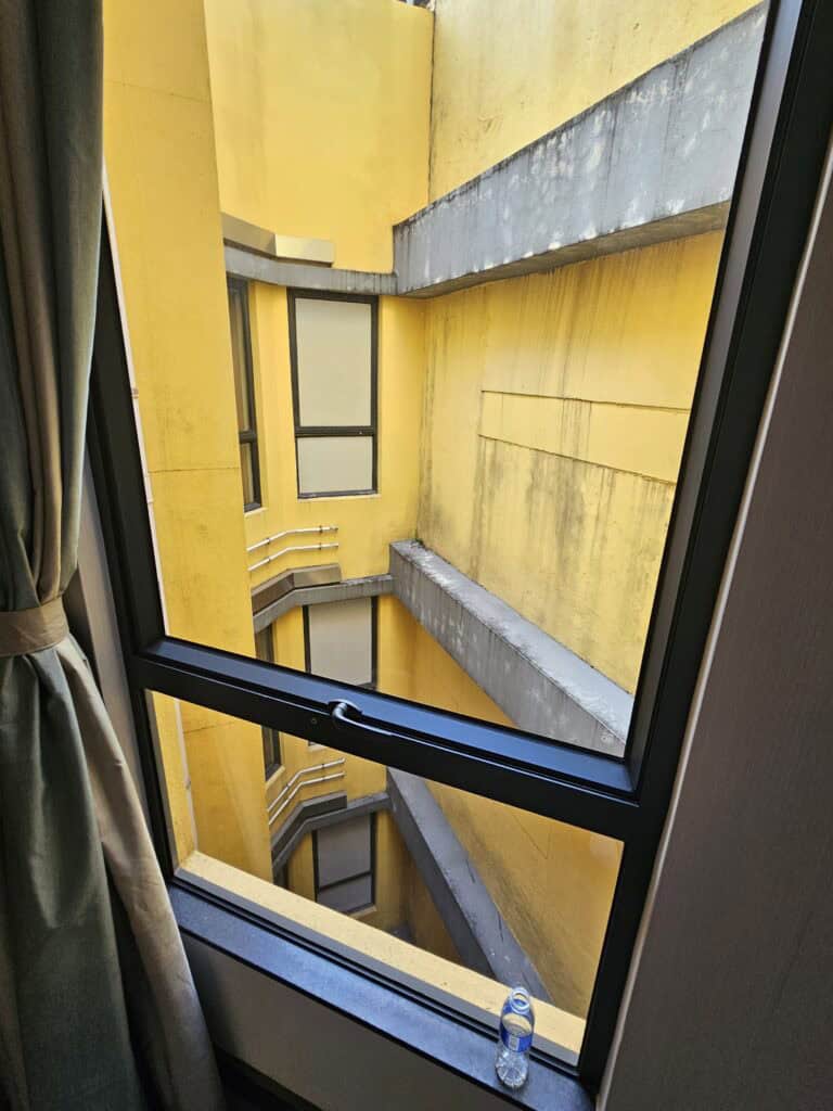 View from a Macau hotel window looking into a narrow yellow building shaft with windows and pipes, showing what some budget room views can look like when choosing where to stay in Macau.