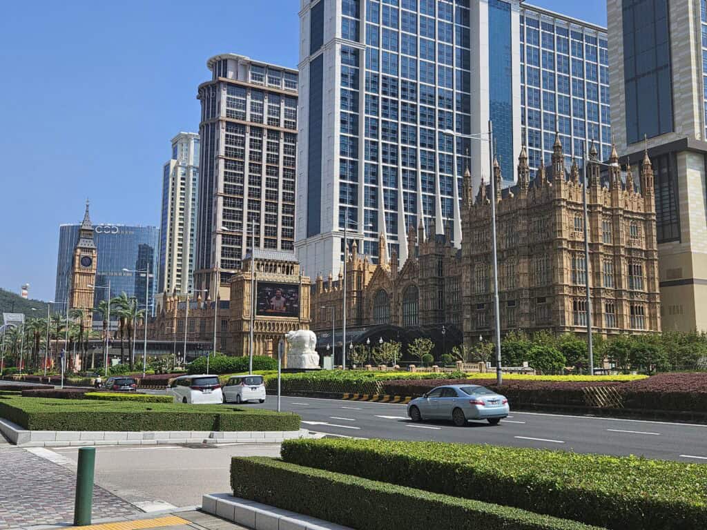 The Londoner Macao resort with detailed historic style architecture and a Big Ben replica surrounded by modern high rise hotels and a busy road. This area highlights the Cotai Strip where many luxury hotels and resorts are located in Macau.