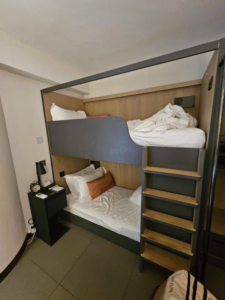 Compact hotel room at BeLive and More in Macau featuring modern bunk beds with a ladder, white bedding, and a small bedside table. The setup shows a space efficient accommodation option suitable for budget travelers.