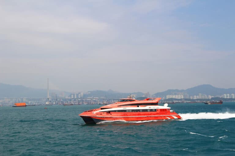Red TurboJET ferry speeding across the water with Hong Kong skyline and bridge in the background, showing what the Hong Kong to Macau ferry looks like during the journey.