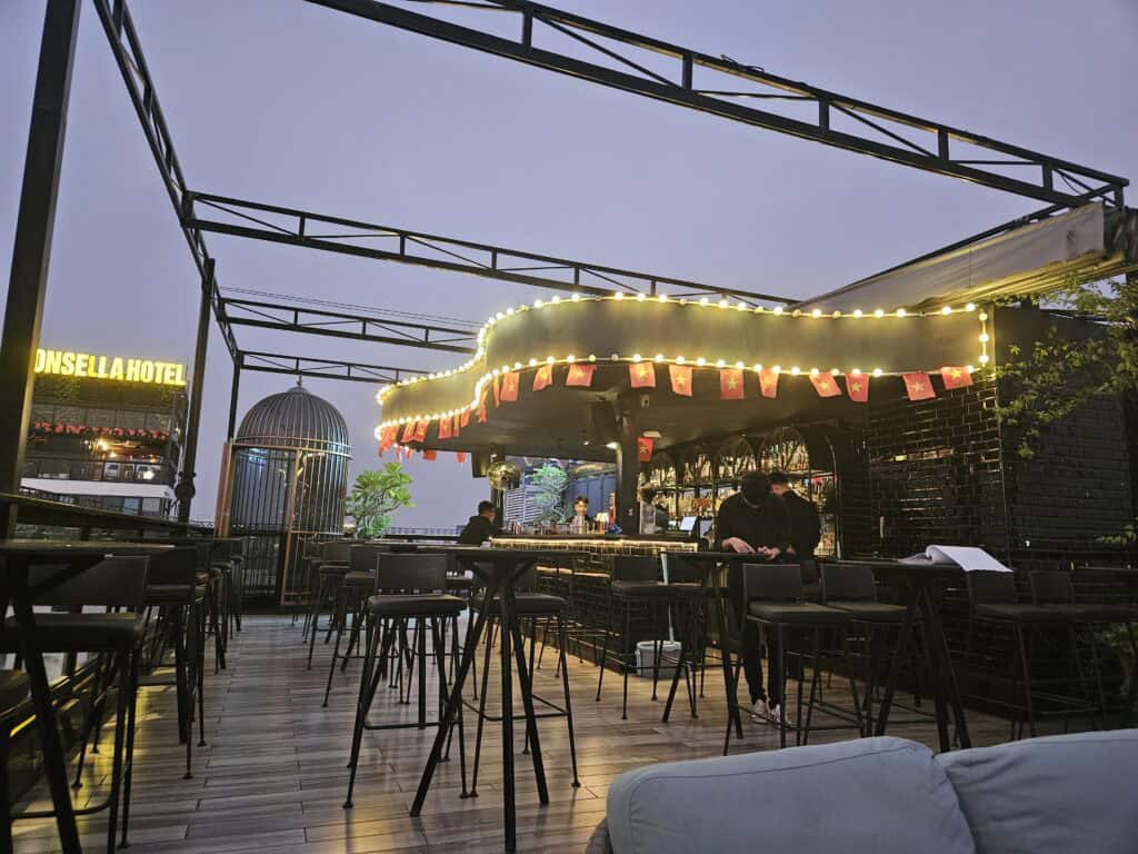 Rooftop bar at Solaria Hotel Hanoi with string lights, high tables, and a lit up bar area decorated with small Vietnamese flags, highlighting on site amenities for where to stay in Hanoi.
