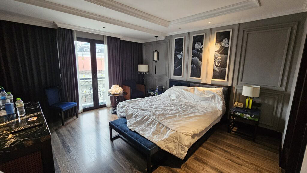 Bedroom at Solaria Hotel Hanoi with a king bed, blue bench, floral wall art, and soft lighting, highlighting comfort and design when deciding where to stay in Hanoi.
