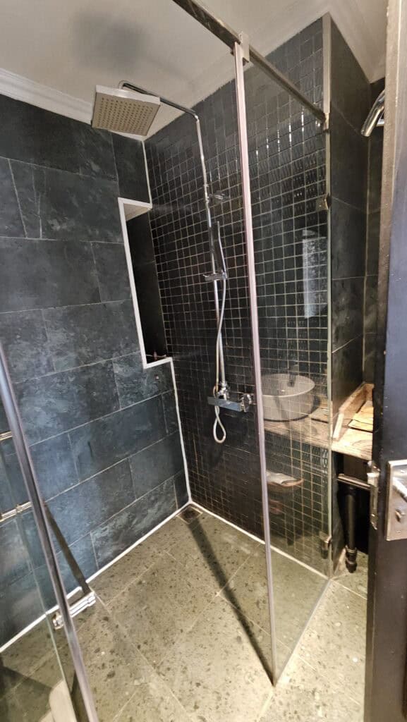 Walk in shower at Solaria Hotel Hanoi with glass enclosure, rainfall showerhead, and dark tiled walls, highlighting modern bathroom features when choosing where to stay in Hanoi.