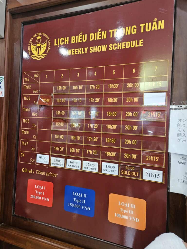 Weekly show schedule board at Thang Long Water Puppet Theatre with performance times listed by day and ticket prices below. Colored boxes show Type I 200,000 VND, Type II 150,000 VND, and Type III 100,000 VND.