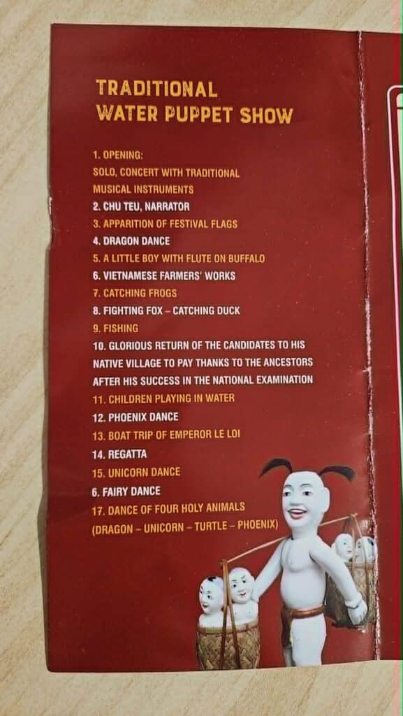 Program page titled "Traditional Water Puppet Show" on a red brochure from Thang Long Water Puppet Theater. The page lists 17 acts including "Dragon Dance," "Fishing," "Children Playing in Water," "Boat Trip of Emperor Le Loi," and "Dance of Four Holy Animals."