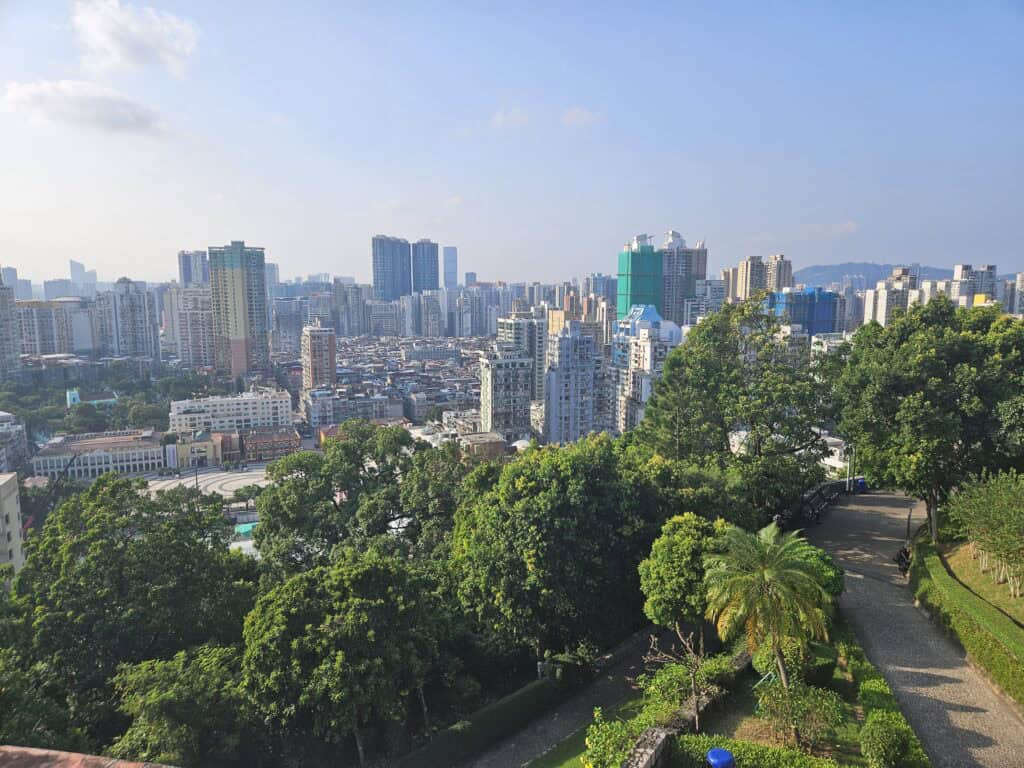 View across Macau from Guia Fortress, with dense apartment towers, green parkland and walking paths overlooking the city skyline.